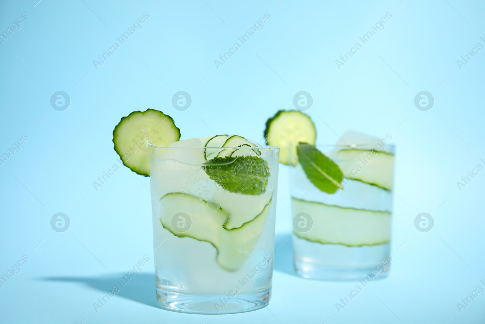 Photo of Tasty fresh cucumber water with mint on light blue background