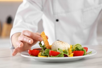 Photo of Professional chef decorating delicious salad with crispy bread at marble table, closeup