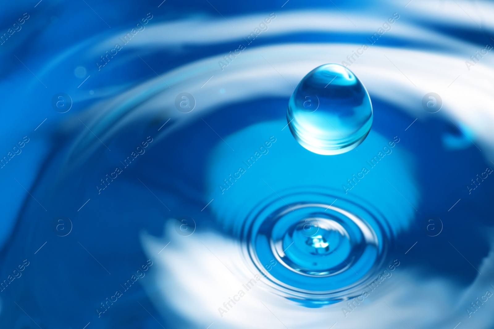 Photo of Drop falling into clear water on blue background, closeup