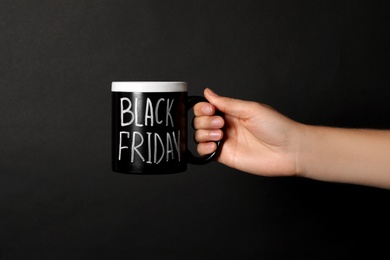 Woman holding cup with phrase Black Friday against dark background, closeup