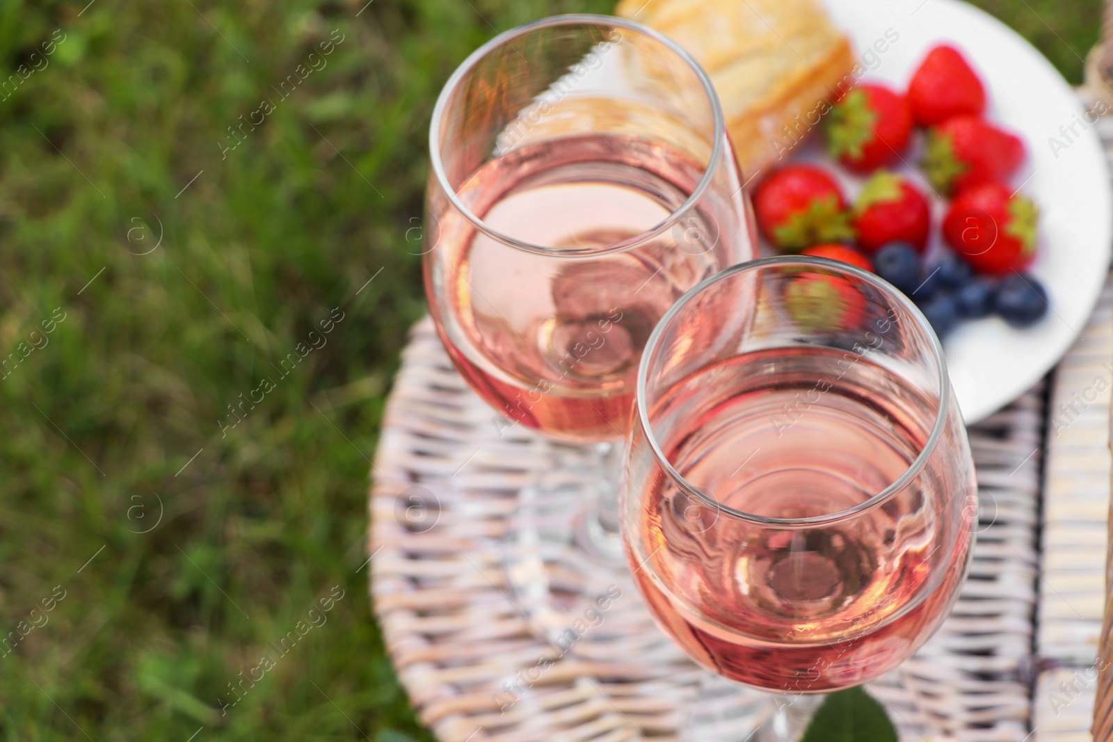 Photo of Glasses of delicious rose wine and food on picnic basket outdoors, closeup. Space for text