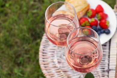 Glasses of delicious rose wine and food on picnic basket outdoors, closeup. Space for text