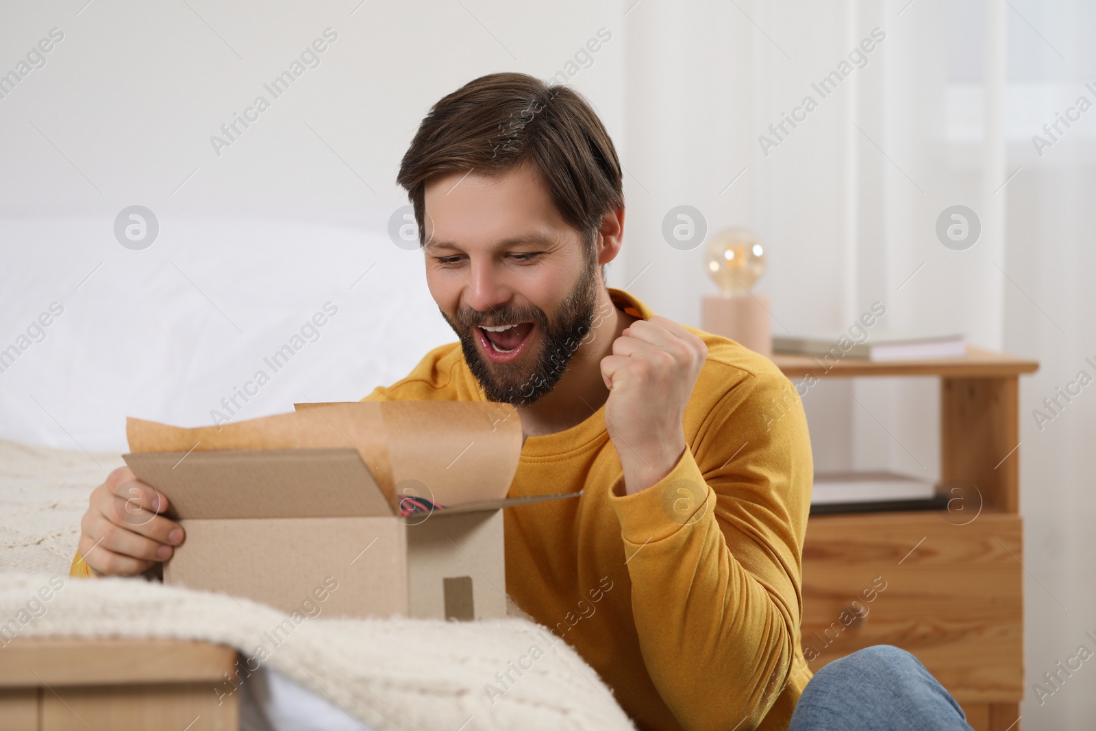 Photo of Happy man opening parcel at home. Internet shopping