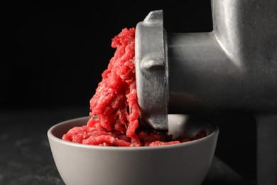 Photo of Mincing beef with metal meat grinder on black background, closeup