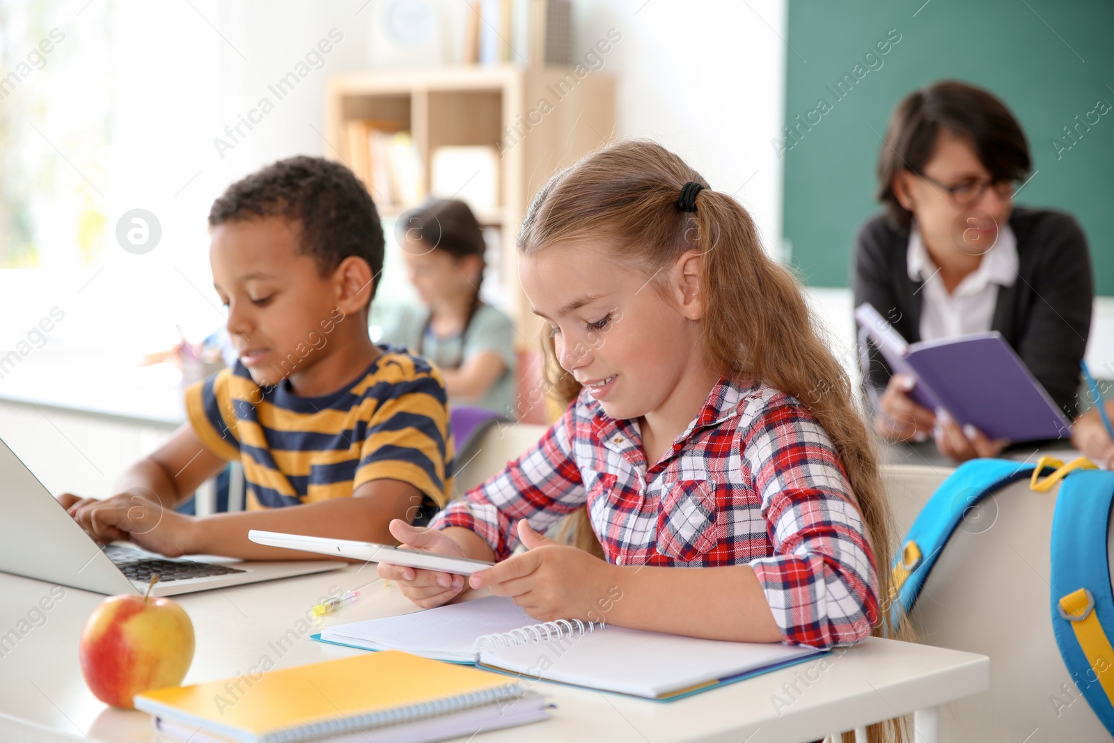 Photo of Cute little children with gadgets sitting at desk in classroom. Elementary school