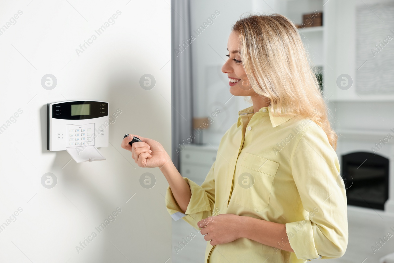 Photo of Home security system. Smiling woman using alarm key fob in room