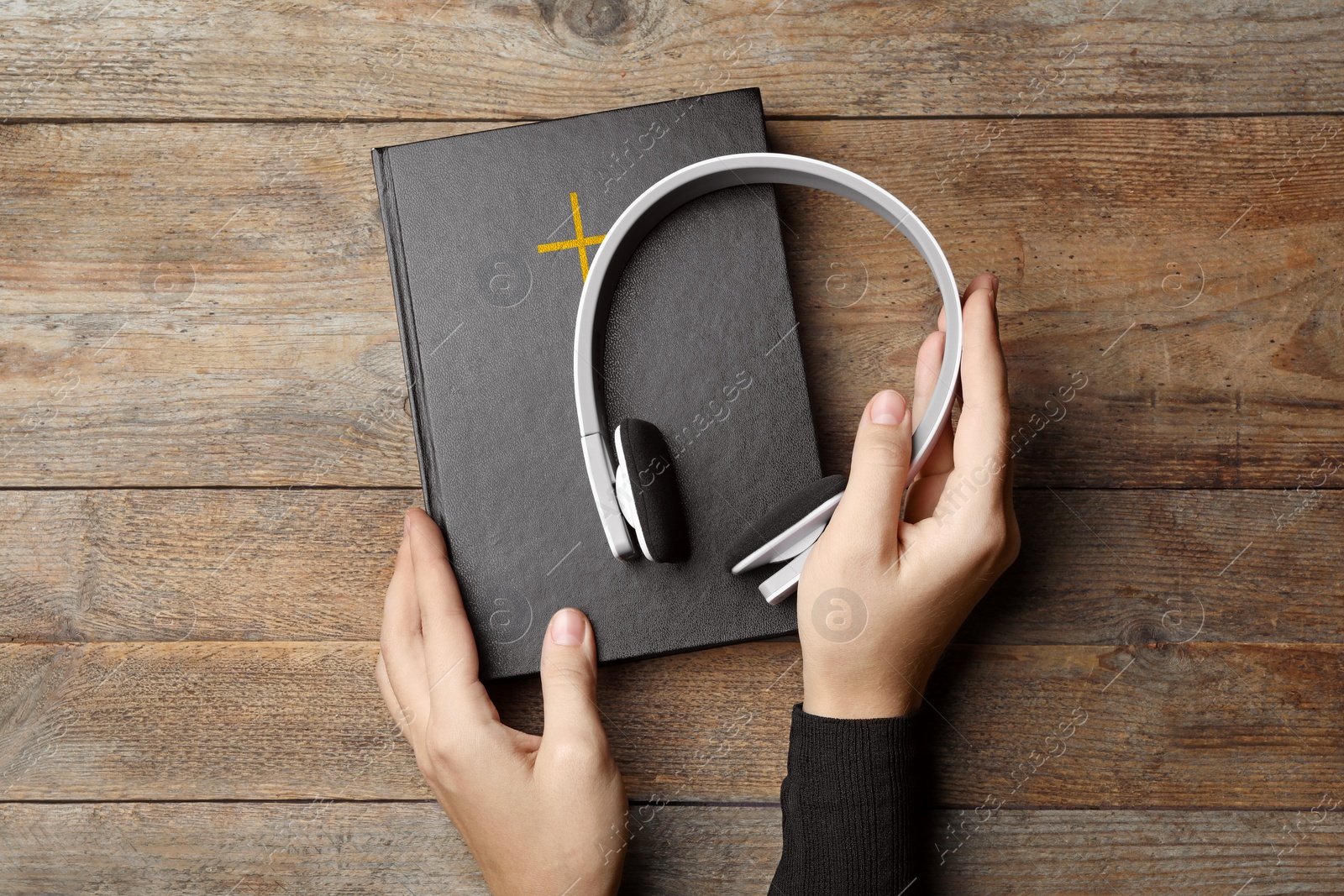 Photo of Woman with Bible and headphones at wooden table, top view. Religious audiobook