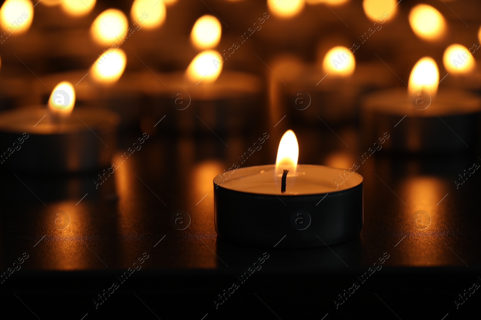 Photo of Burning tealight candles on dark surface, closeup