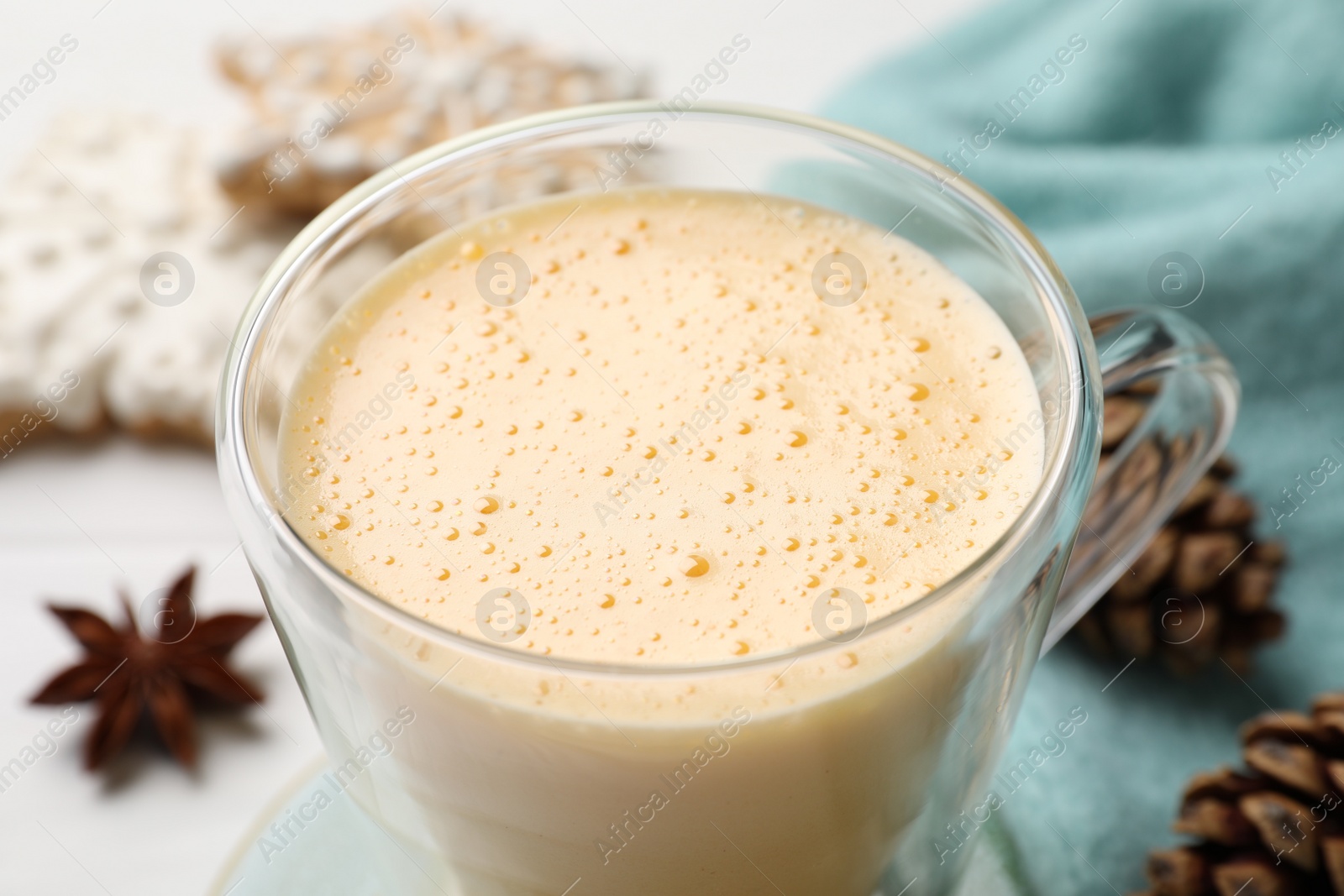 Photo of Glass cup with tasty eggnog on white table, closeup