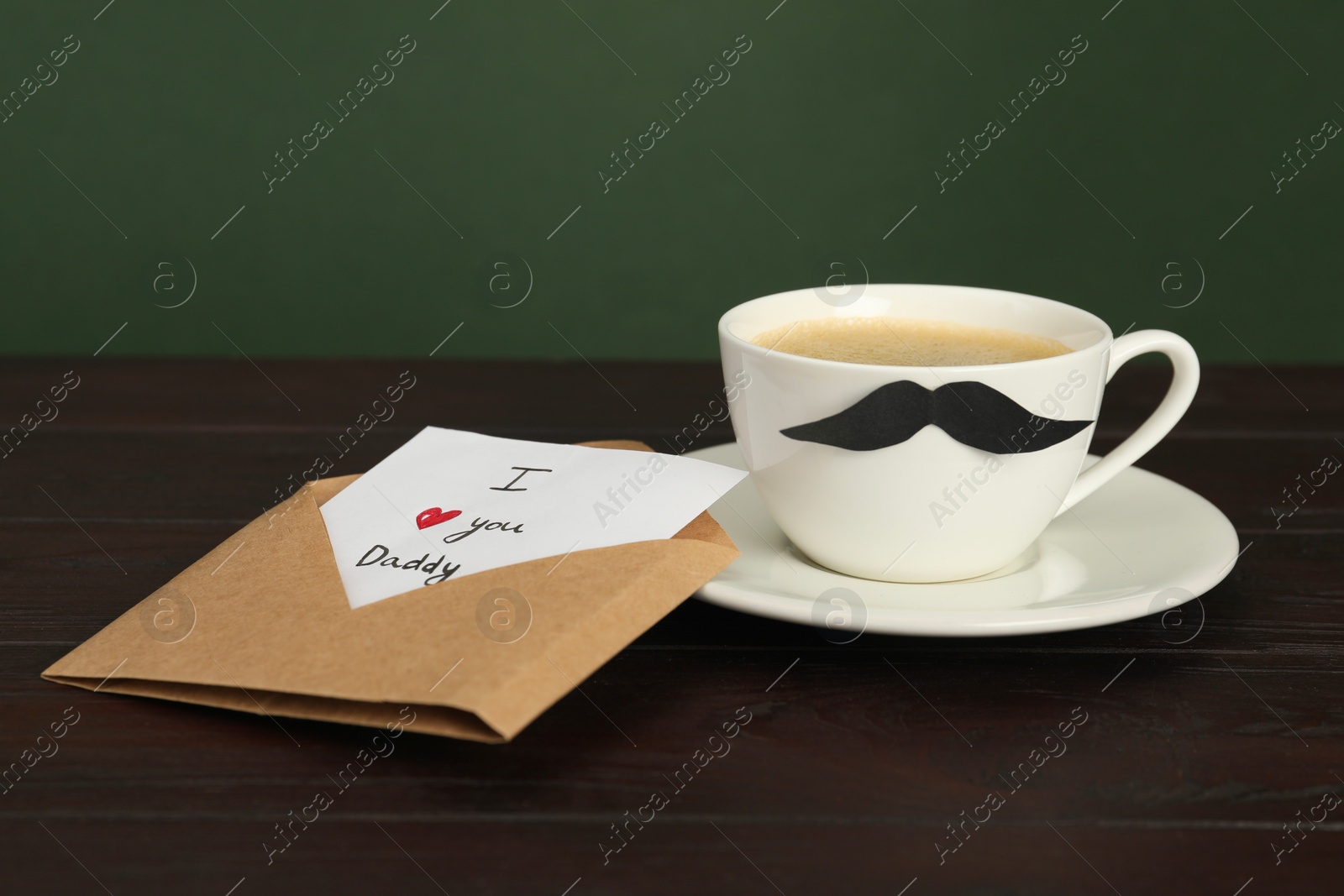 Photo of Happy Father's Day. Card with phrase I Love You, Daddy in envelope and cup of coffee on wooden table, closeup