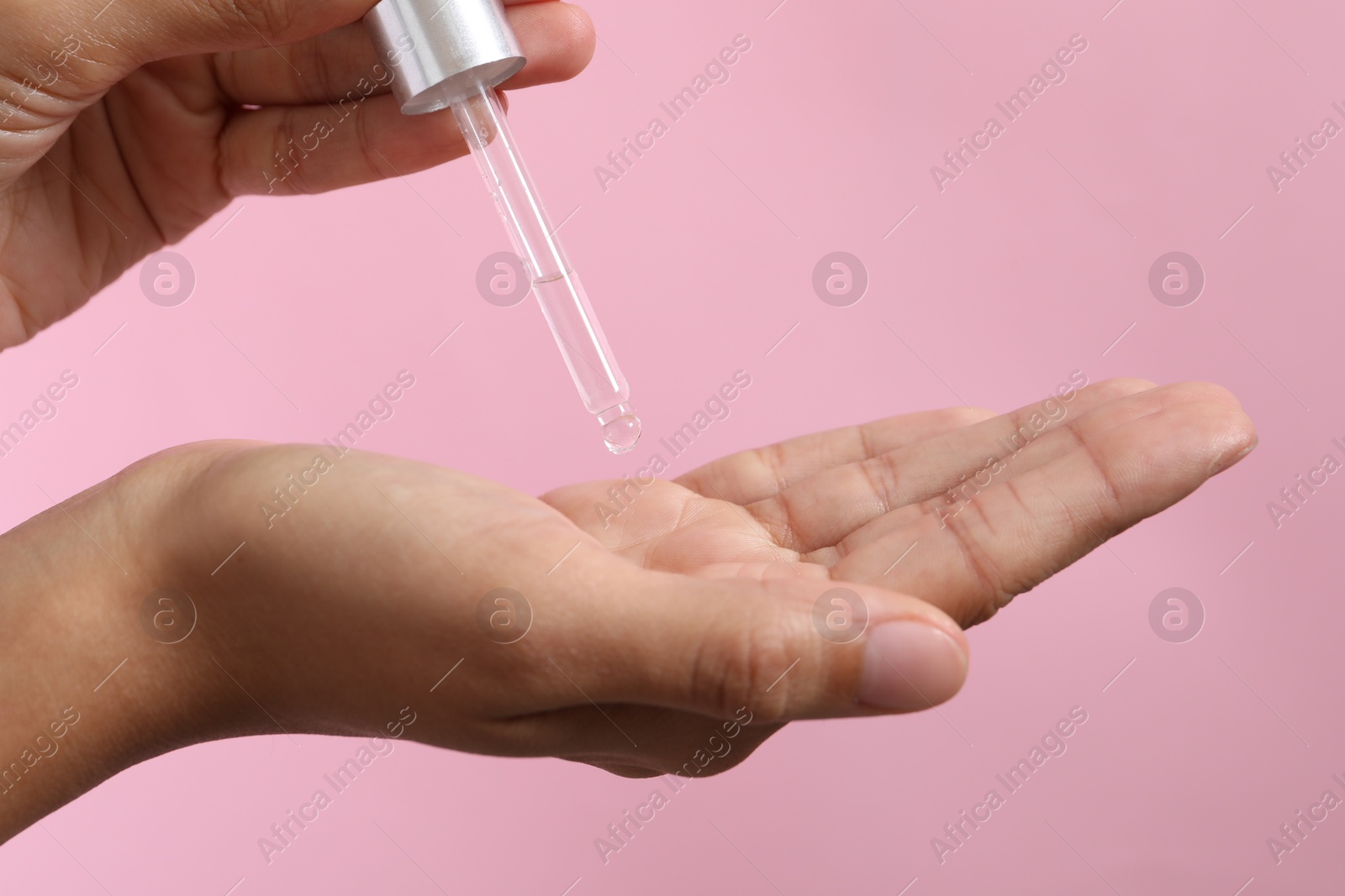 Photo of Woman applying cosmetic serum onto her hand on pink background, closeup