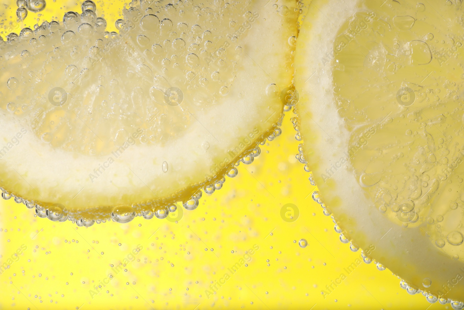 Photo of Juicy lemon slices in soda water against yellow background, closeup