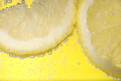 Juicy lemon slices in soda water against yellow background, closeup