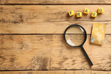 Photo of Word Fraud of yellow cubes with letters , credit card and magnifying glass on wooden background, flat lay. Space for text