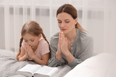 Girl and her godparent praying over Bible together at home