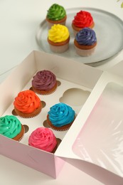 Box with delicious colorful cupcakes on white table