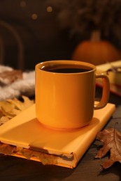 Cup of aromatic tea, book and autumn leaves on wooden table indoors, closeup