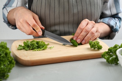 Woman cutting curly parsley at light grey table, closeup