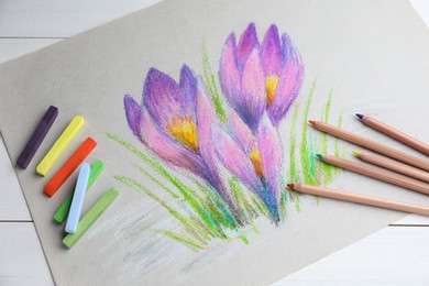 Photo of Colorful chalk pastels, pencils and beautiful painting of crocus flowers on white wooden table, above view