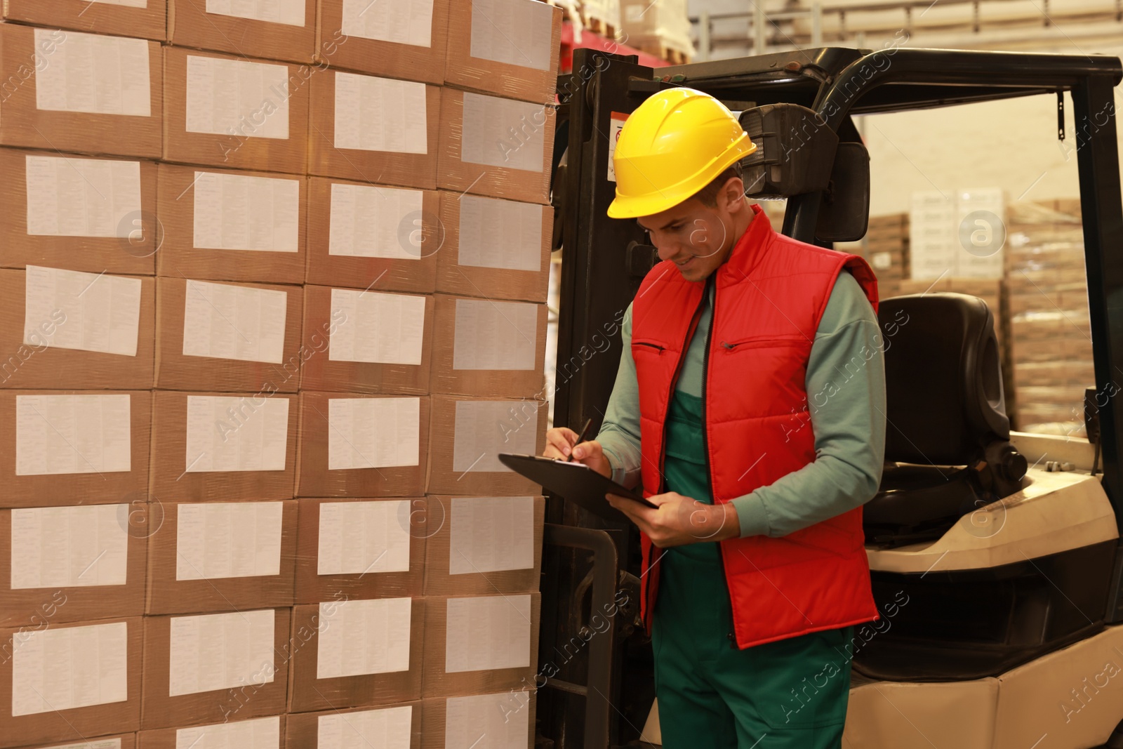 Image of Worker near forklift truck with cardboard boxes in warehouse. Logistics concept