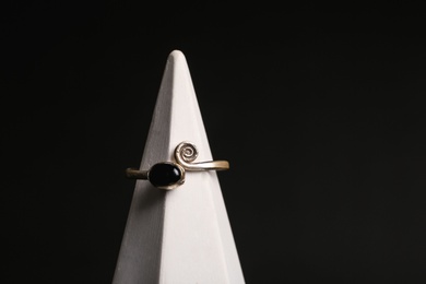 Stylish ring on stand against black background, space for text. Luxury jewelry