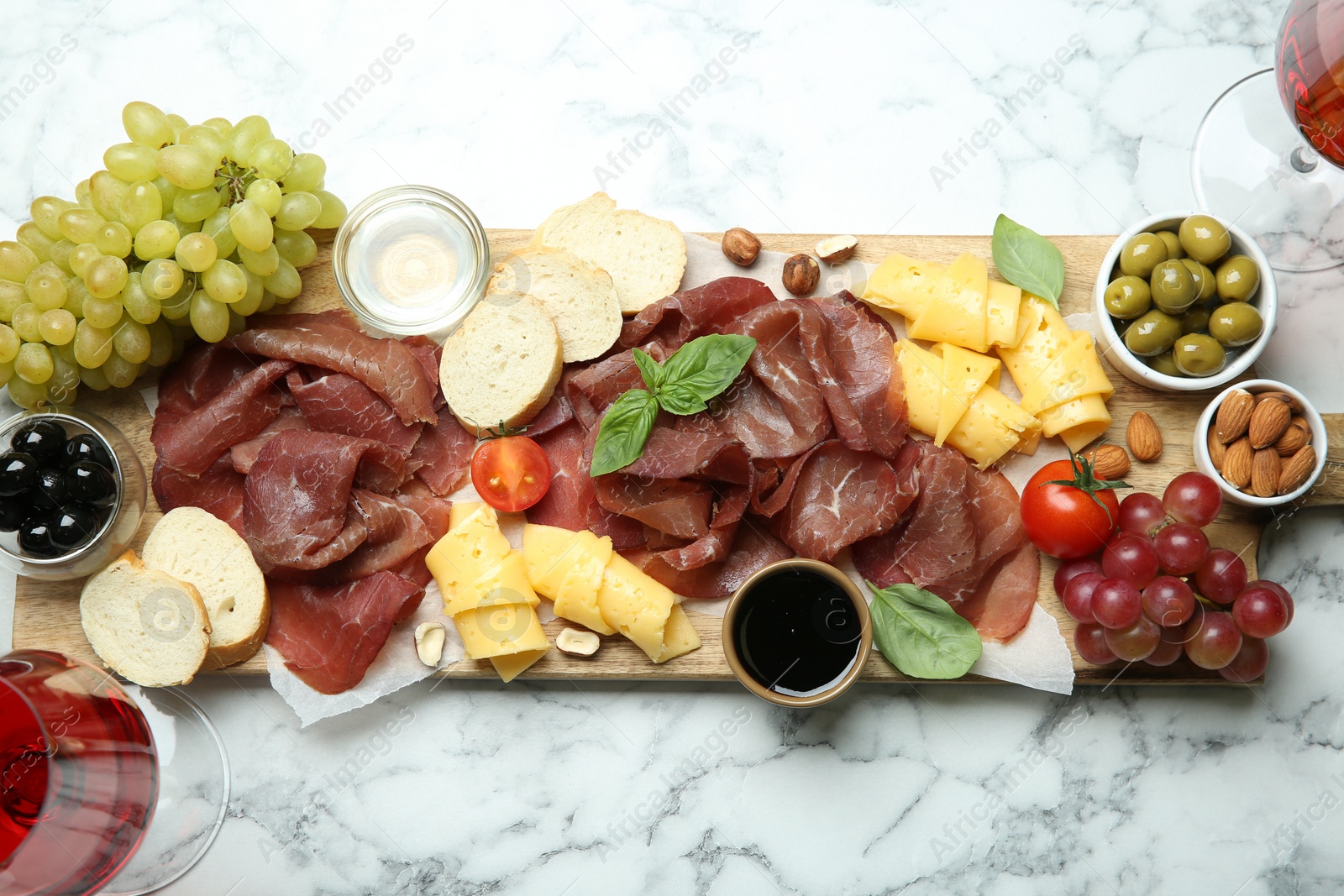 Photo of Charcuterie board. Delicious bresaola and other snacks on white marble table, top view