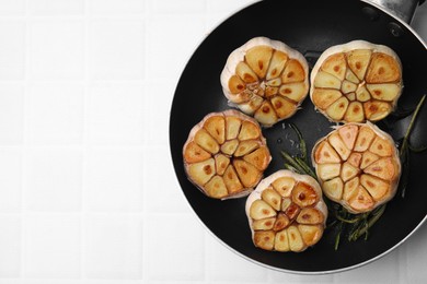 Frying pan with fried garlic and rosemary on white tiled table, top view. Space for text