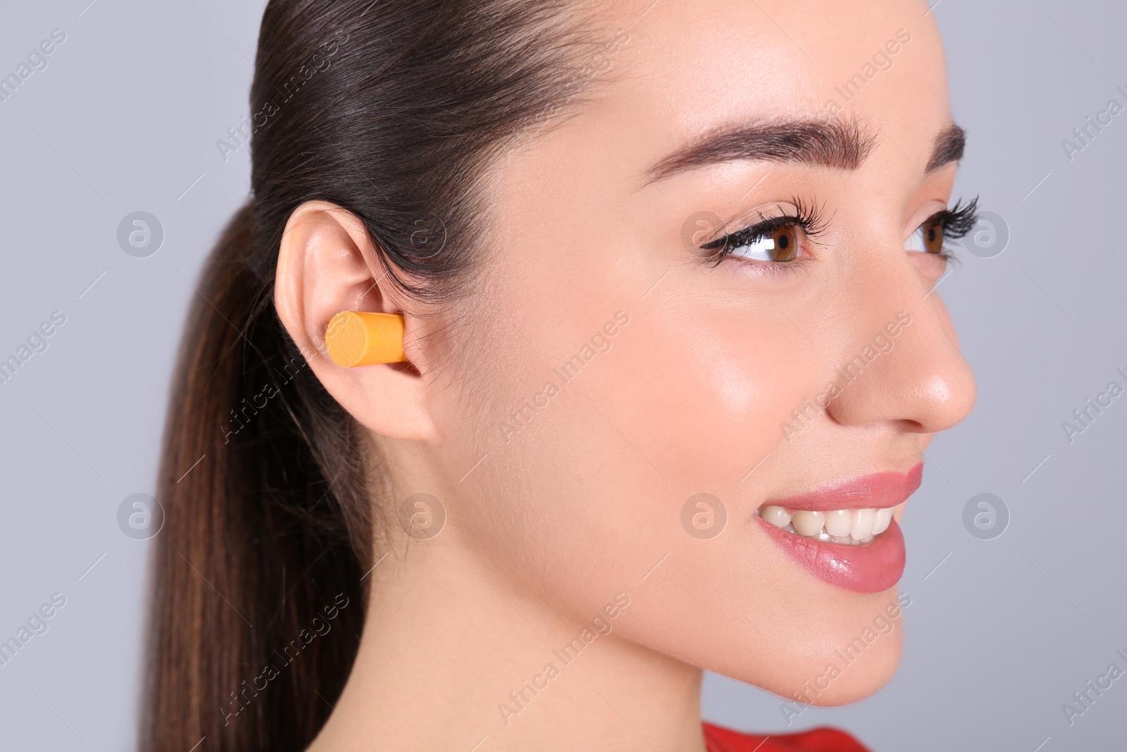Photo of Young woman wearing foam ear plug on grey background, closeup