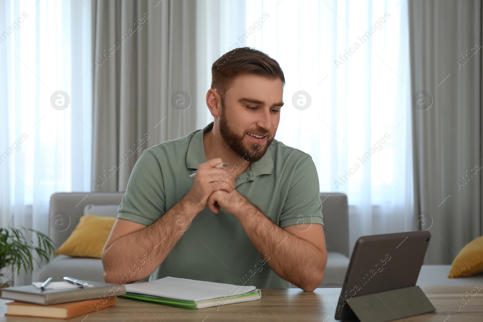 Photo of Young man watching online webinar at table indoors