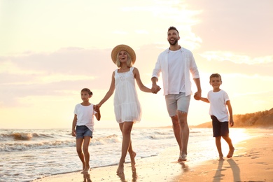 Photo of Happy family walking on sandy beach near sea at sunset