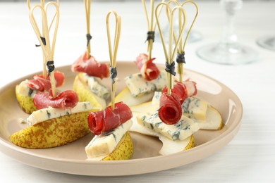 Photo of Tasty canapes with pears, blue cheese and prosciutto on white wooden table, closeup