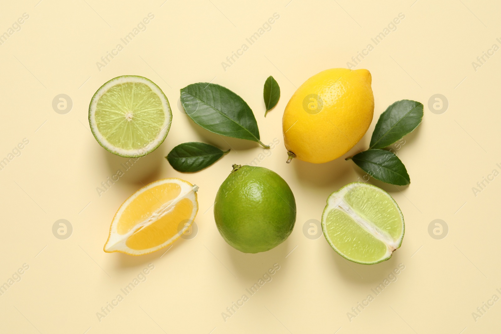 Photo of Fresh ripe lemons, limes and green leaves on beige background, flat lay