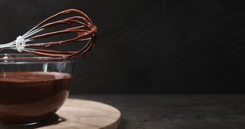 Bowl and whisk with yummy chocolate cream on black table, closeup. Banner design with space for text