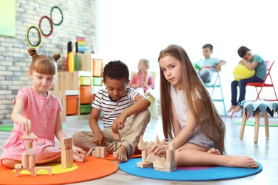 Photo of Cute little children playing with wooden blocks indoors