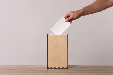 Man putting his vote into ballot box on light grey background, closeup