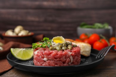 Photo of Tasty beef steak tartare served with quail egg and other accompaniments on wooden table