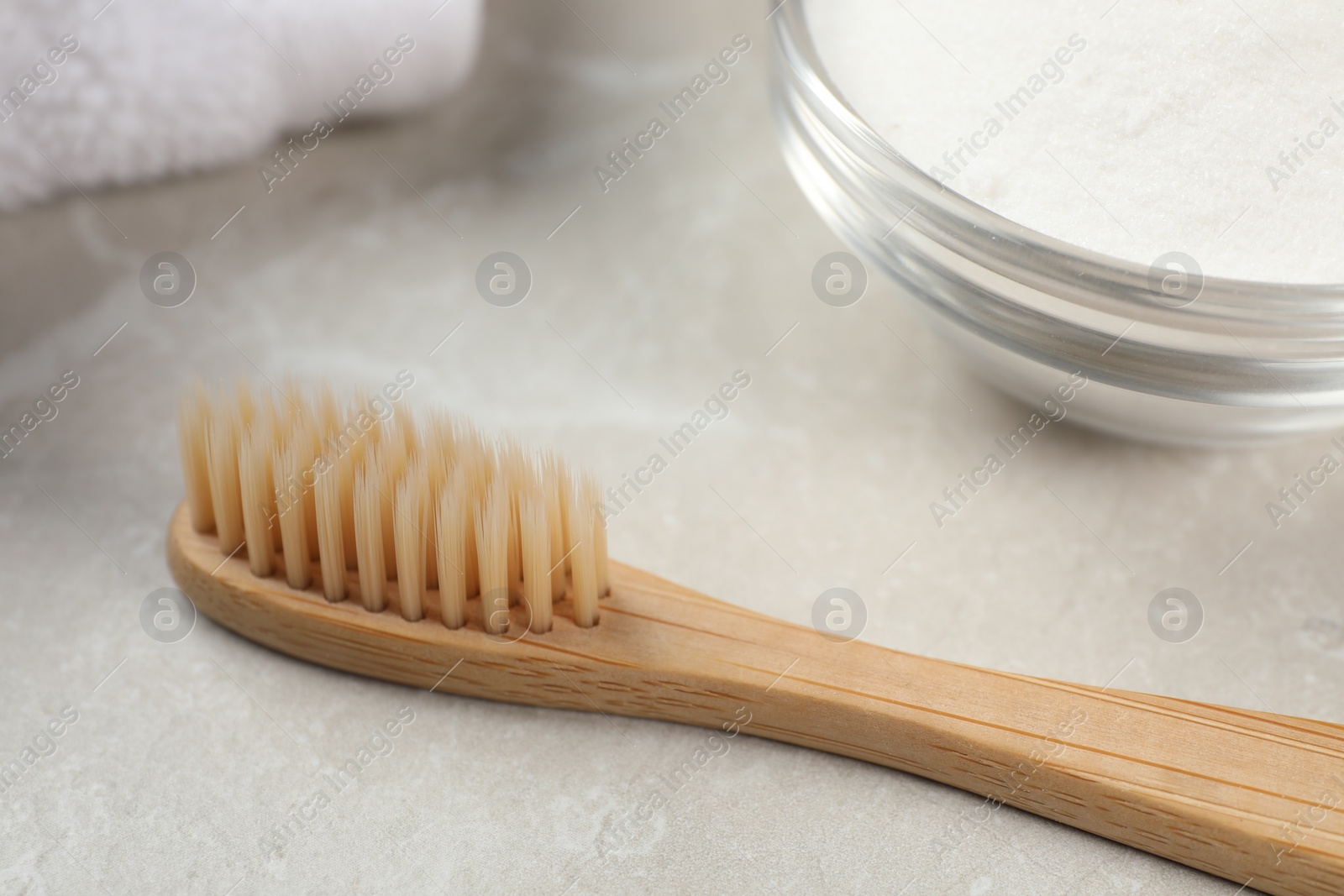 Photo of Bamboo toothbrush and glass bowl of baking soda on light grey marble table, closeup