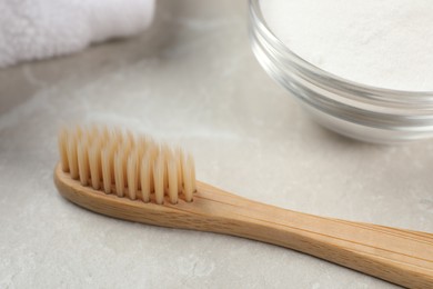 Bamboo toothbrush and glass bowl of baking soda on light grey marble table, closeup