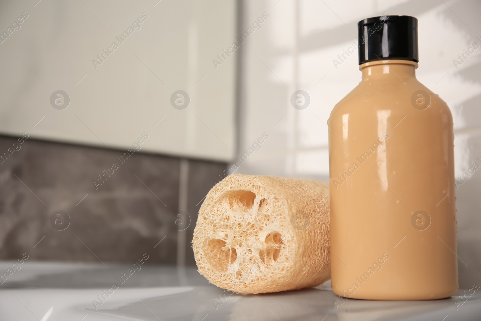 Photo of Natural loofah sponge and shower gel bottle on washbasin in bathroom, closeup. Space for text