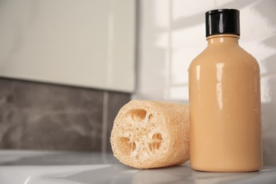 Natural loofah sponge and shower gel bottle on washbasin in bathroom, closeup. Space for text