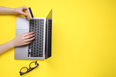 Online payment. Woman with laptop, credit card and glasses on yellow background, top view. Space for text