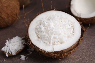 Photo of Coconut flakes in nut shell and spoon on brown table, closeup