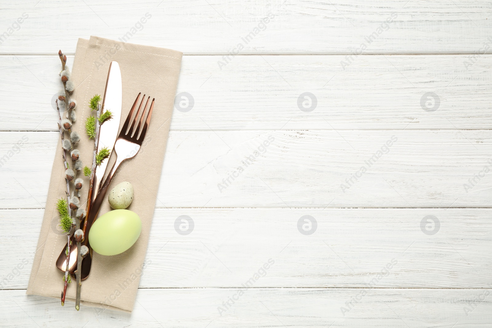 Photo of Cutlery set and beautiful willow branches on white wooden table, top view with space for text. Easter celebration