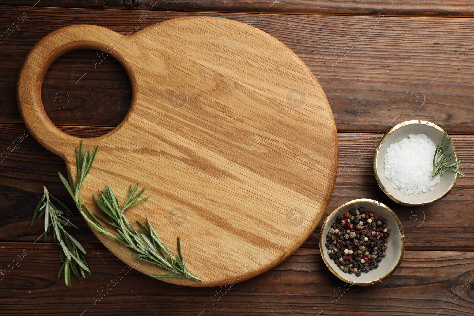 Photo of Cutting board, salt, pepper and rosemary on wooden table, flat lay. Space for text