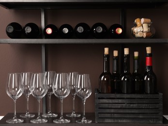 Bottles of wine, corks and glasses on rack near brown wall