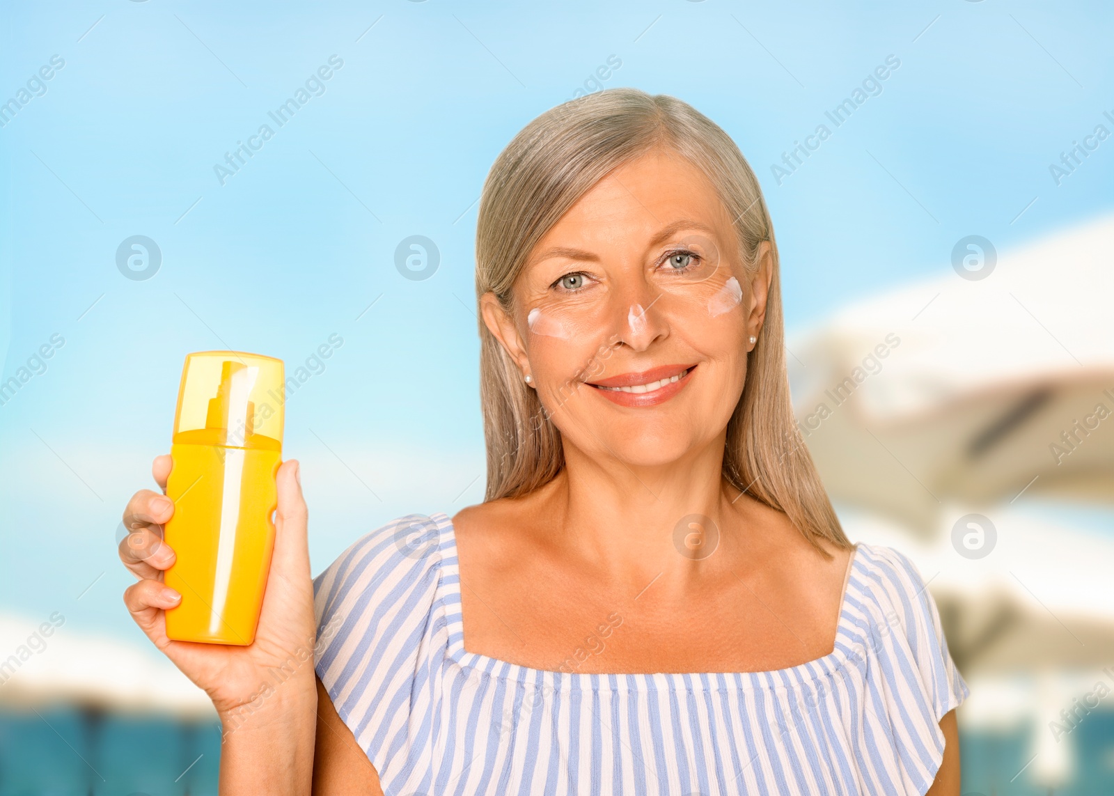 Image of Sun protection. Beautiful mature woman with bottle of sunblock on beach