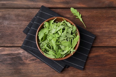 Fresh arugula leaves in bowl on wooden table, flat lay