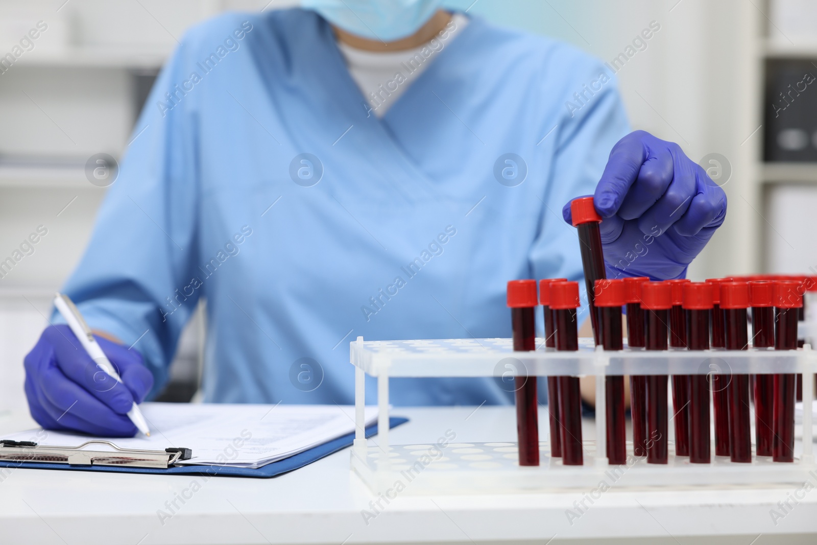 Photo of Laboratory testing. Doctor with blood samples in tubes at white table indoors, closeup