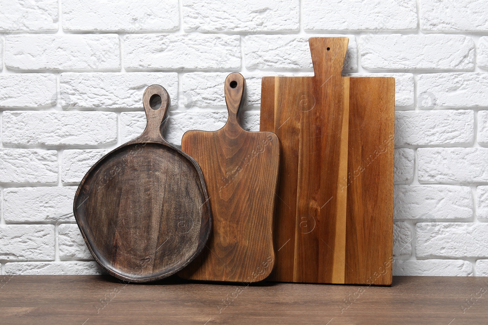 Photo of Different cutting boards on wooden table near white brick wall