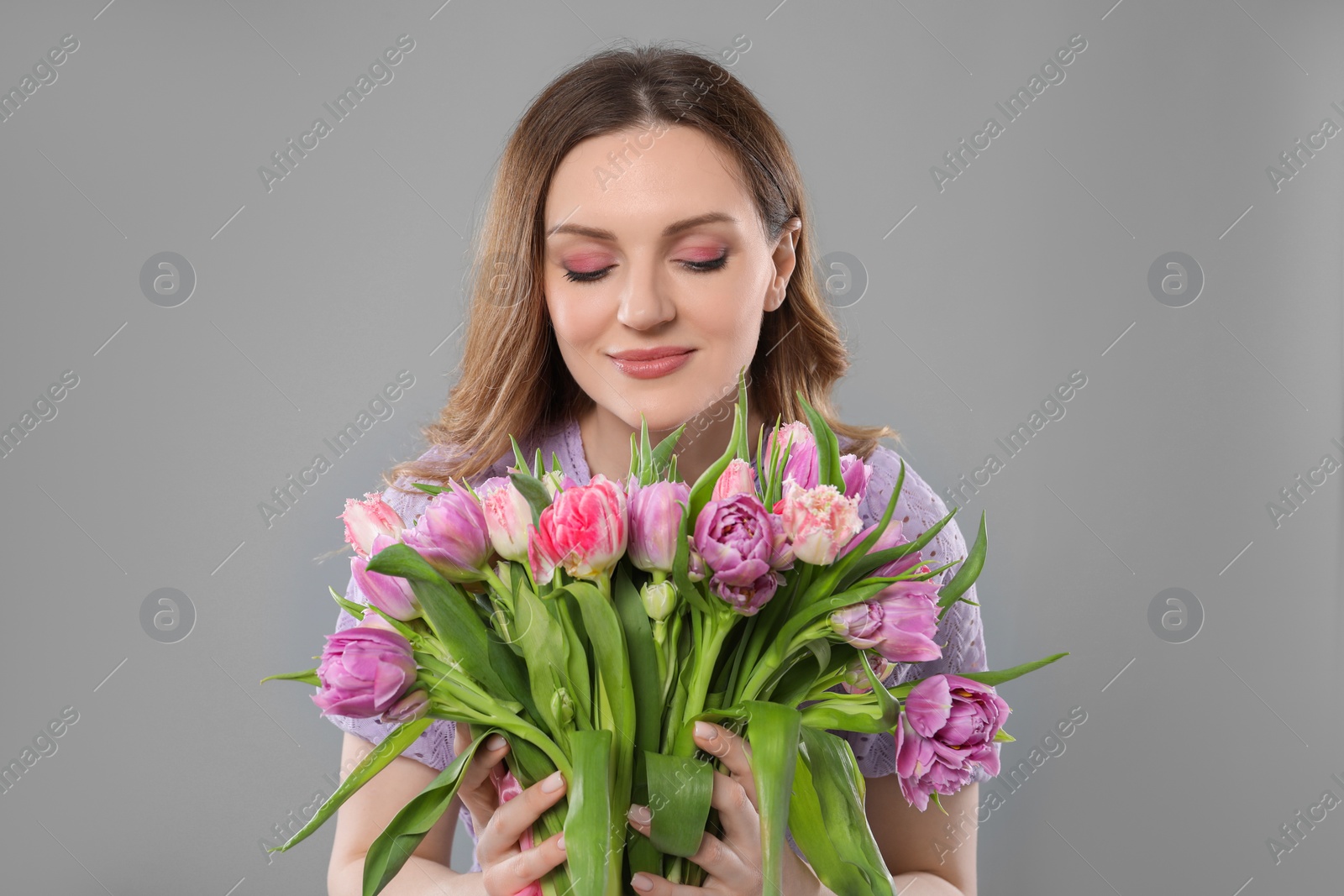 Photo of Happy young woman with bouquet of beautiful tulips on grey background